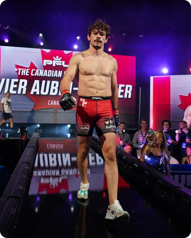 A male MMA fighter in red shorts and gloves walks down an entrance ramp at a PFL event.