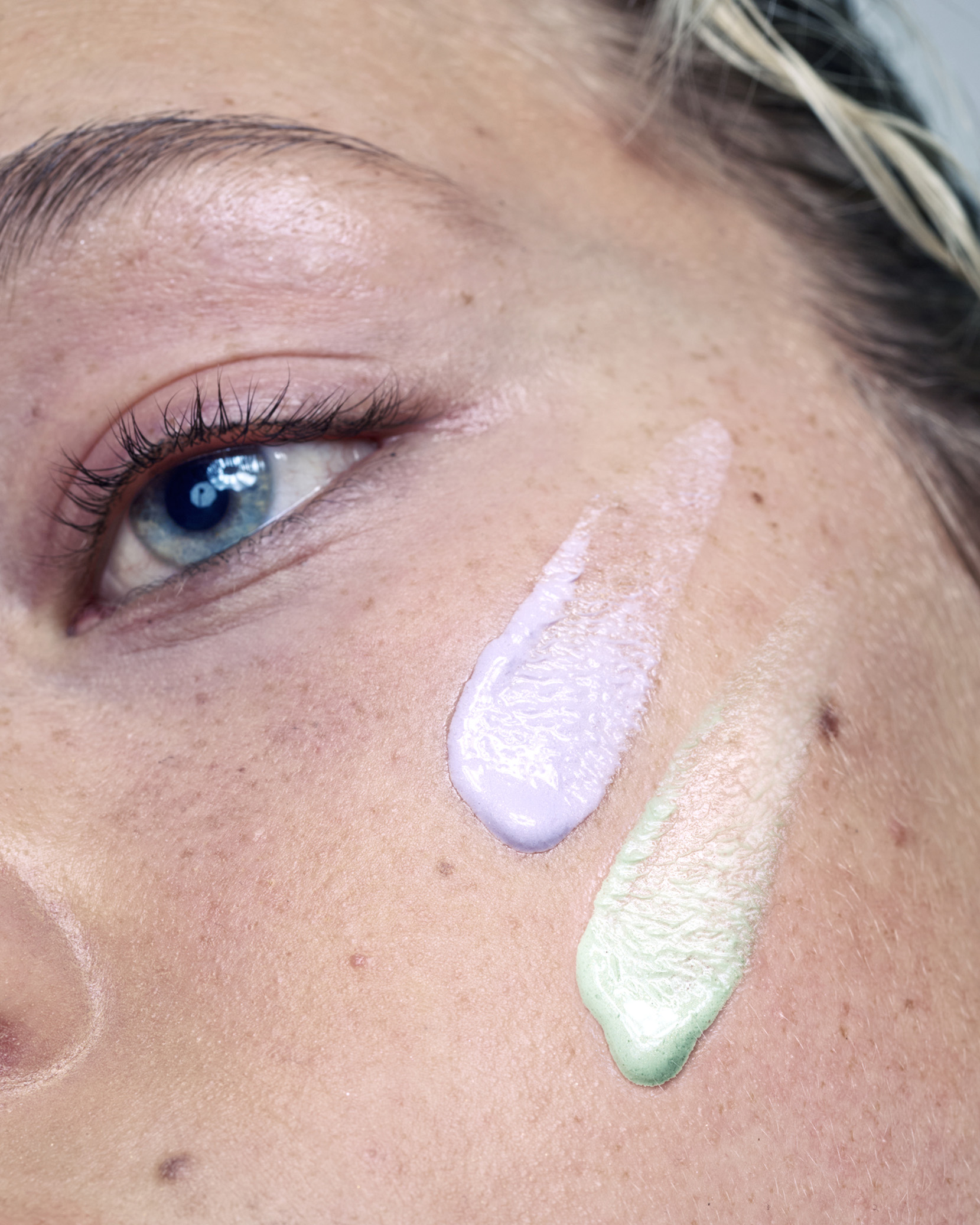 Close-up of a face with purple and green cream on the cheek.