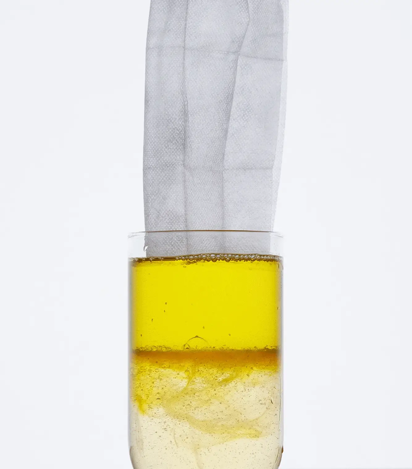 A glass with yellow liquid and a white cloth partially submerged.