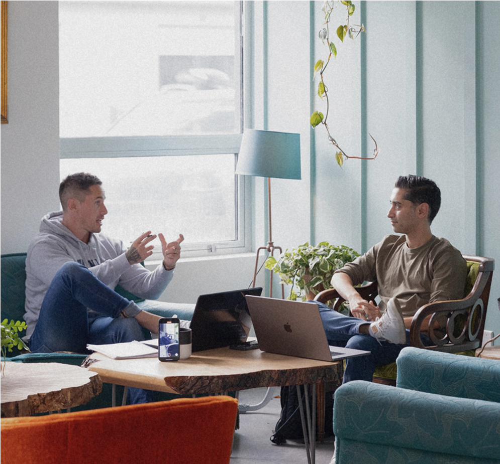 Two people sitting in a modern office, discussing with laptops on a wooden table.