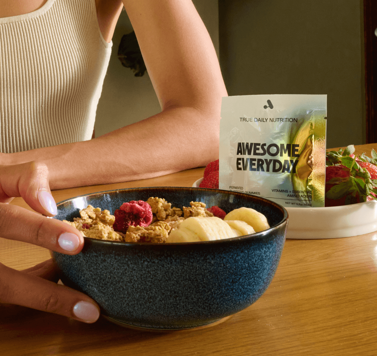 Person holding a bowl with granola, banana slices, and a packet labeled 'Awesome Everyday' visible.