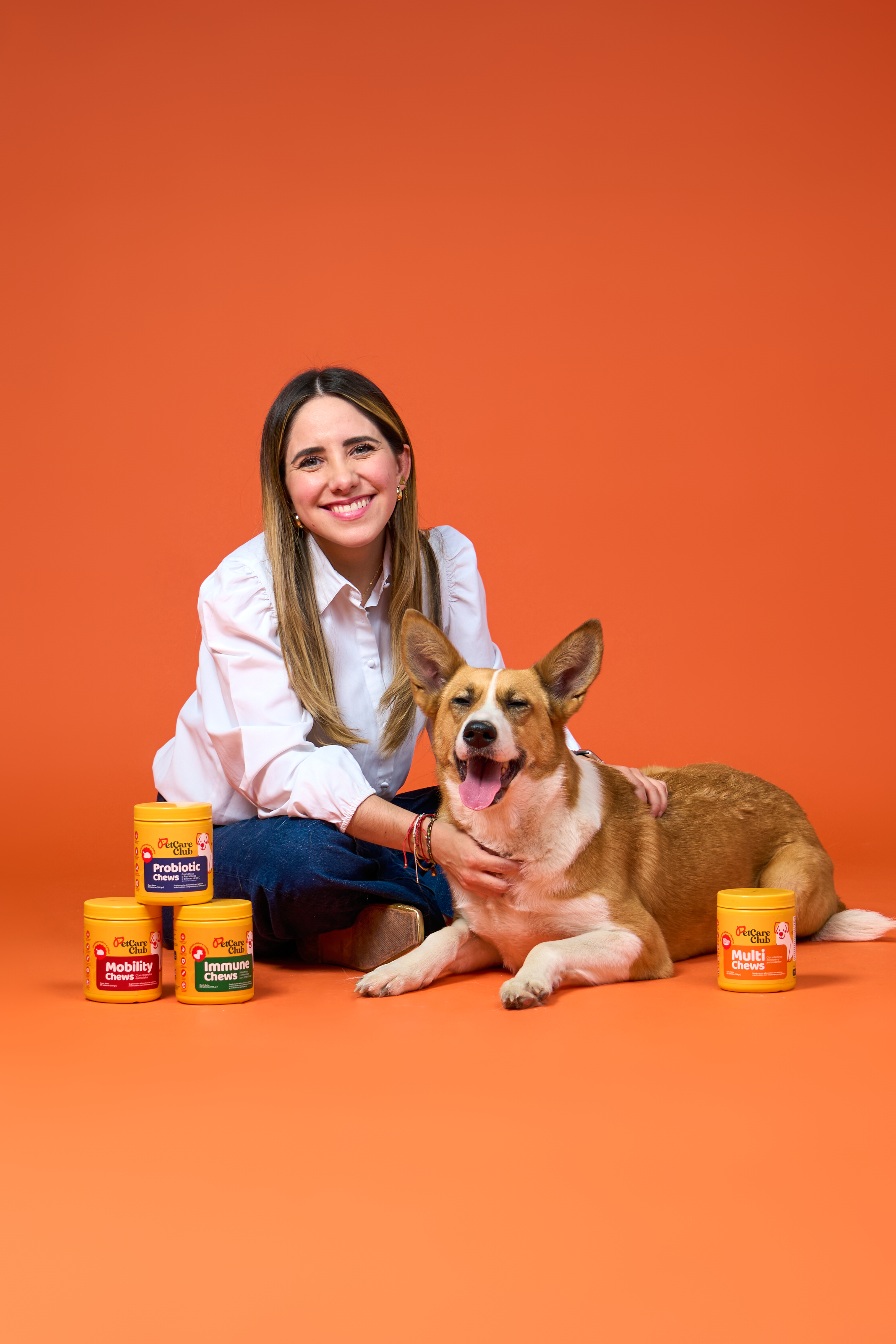 Woman smiling with a dog, surrounded by pet supplement containers on an orange background.