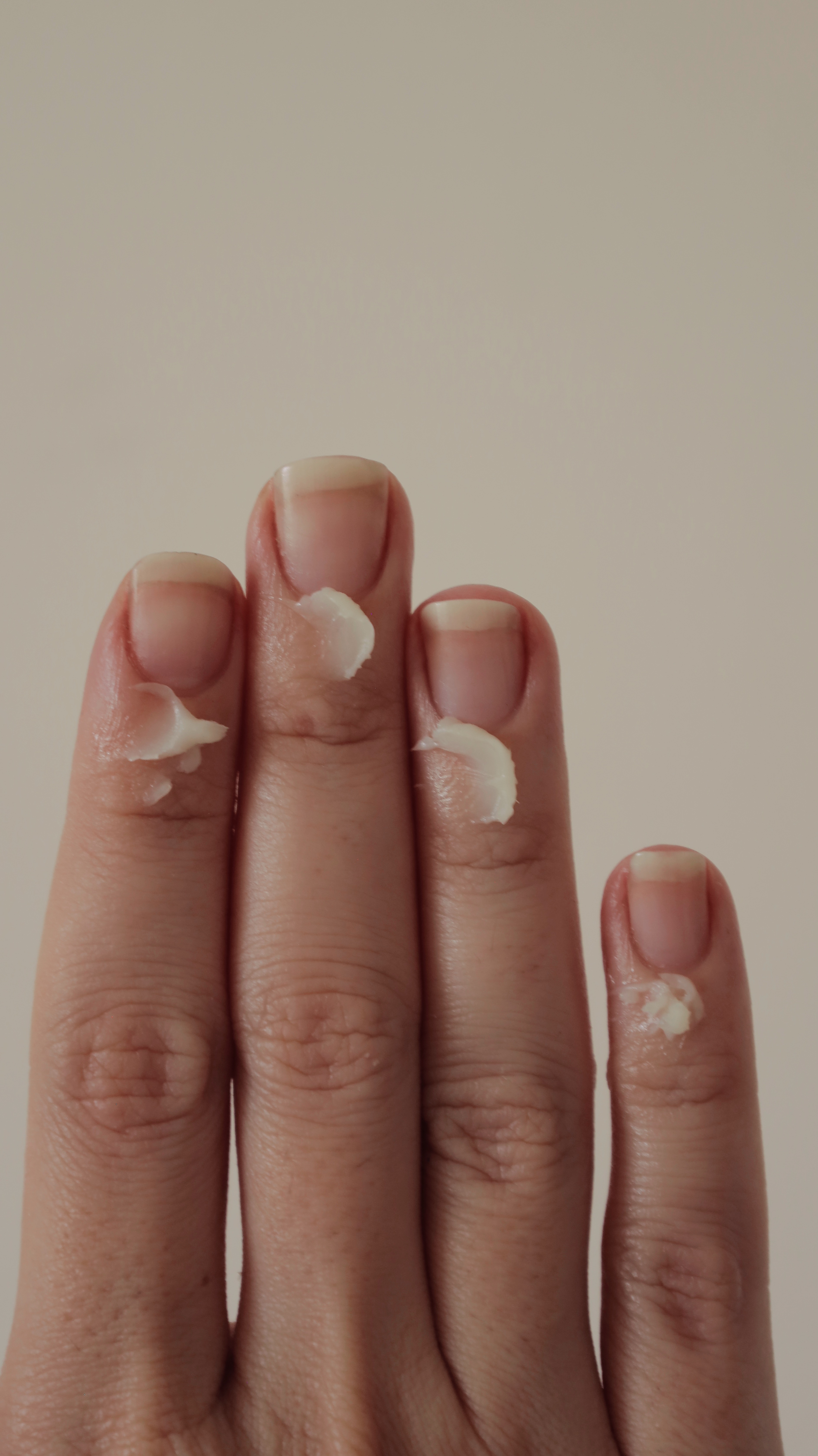 Fingers with cream applied on the nails against a plain background.