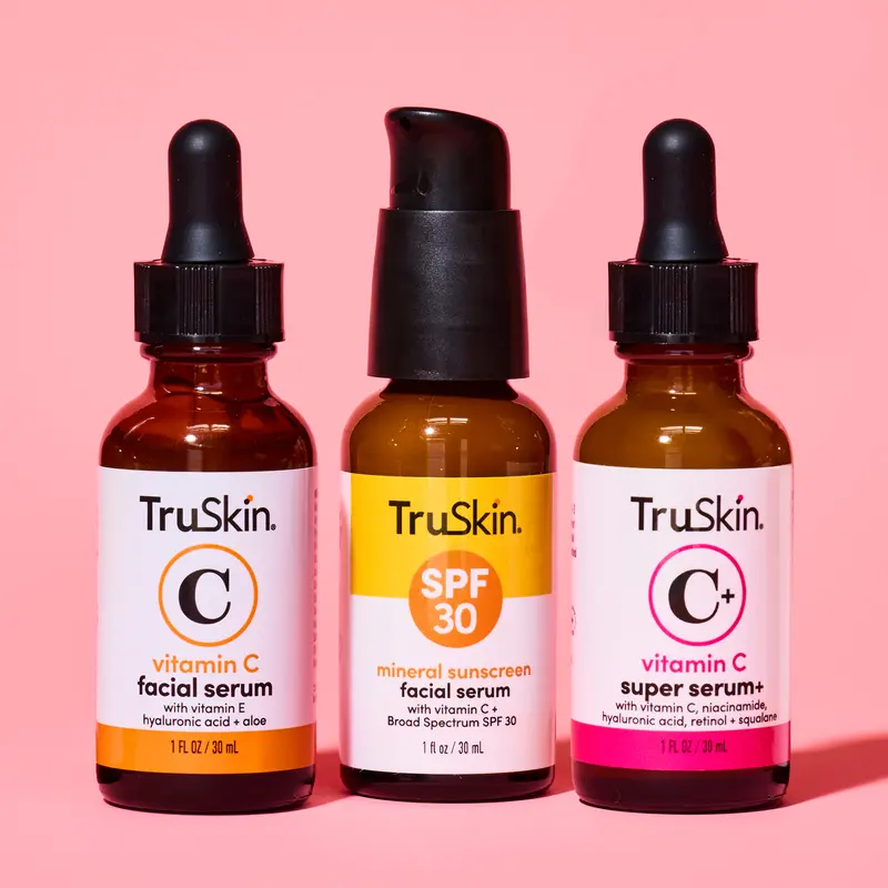 Three bottles of TruSkin brand facial serums are lined up against a pink background.