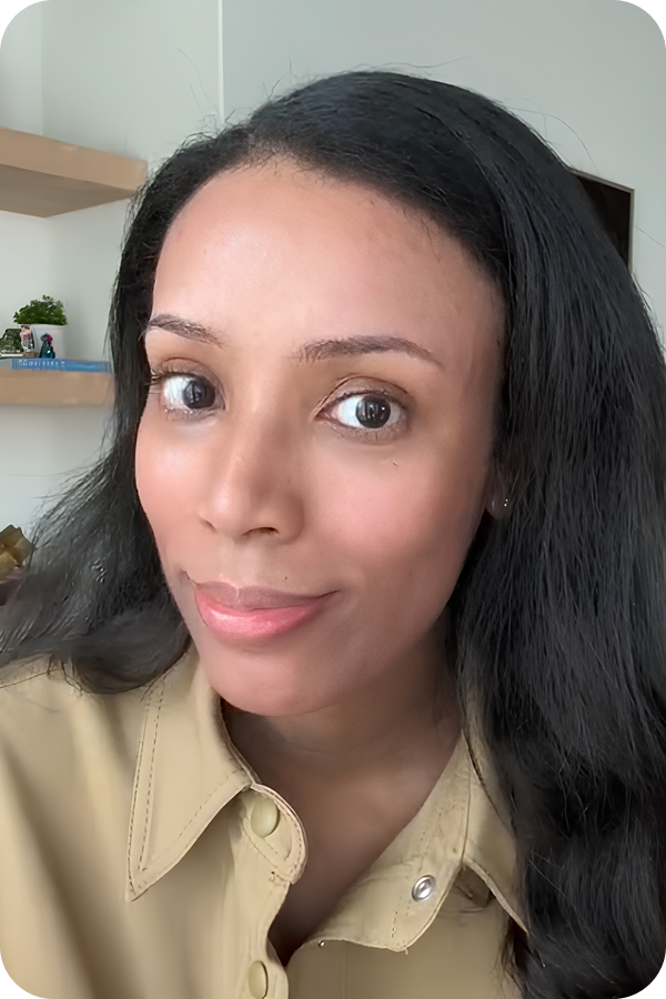 A close-up photo of a woman with long dark hair, wearing a tan shirt, looking at the camera.
