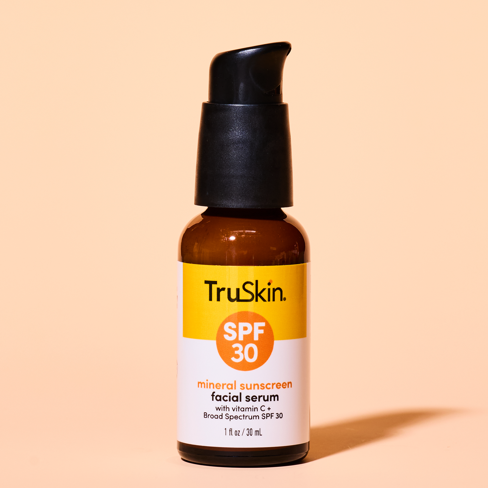 A brown bottle of TruSkin Mineral Sunscreen Facial Serum SPF 30 on a peach background.