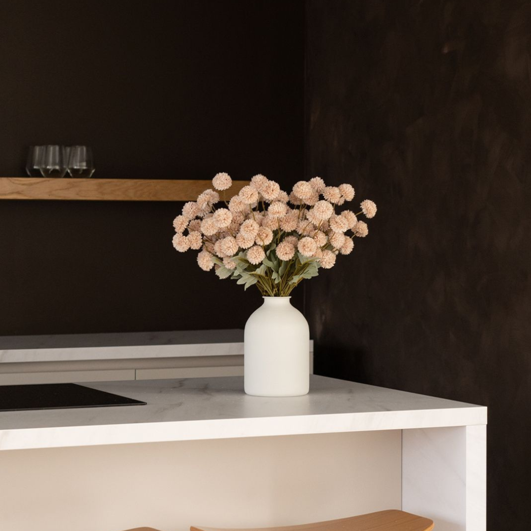 White vase with pink flowers on a marble countertop in a dark room.