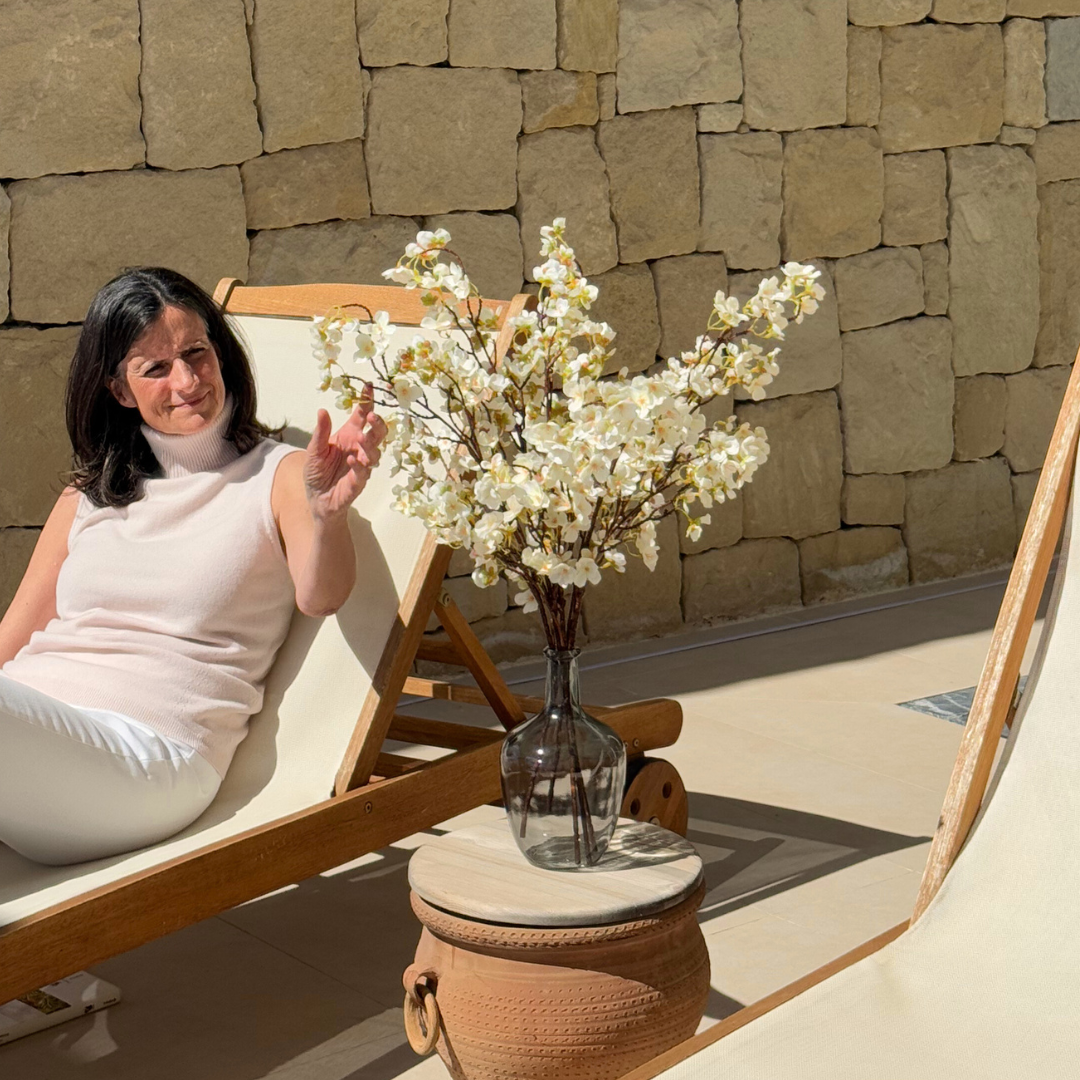 Woman sitting on a lounge chair next to a vase of white flowers.