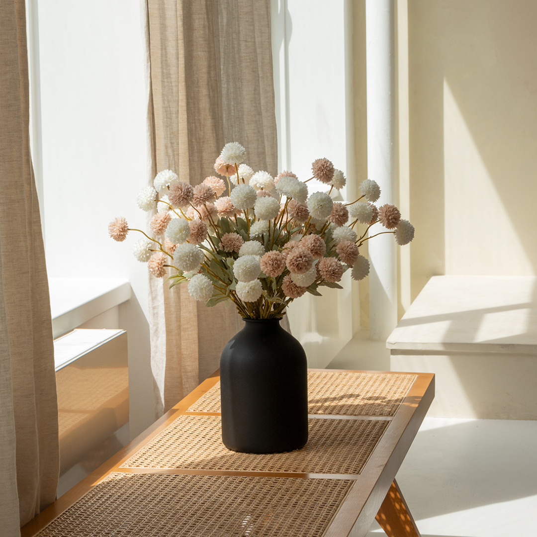 A black vase with white and pink flowers on a sunlit table.