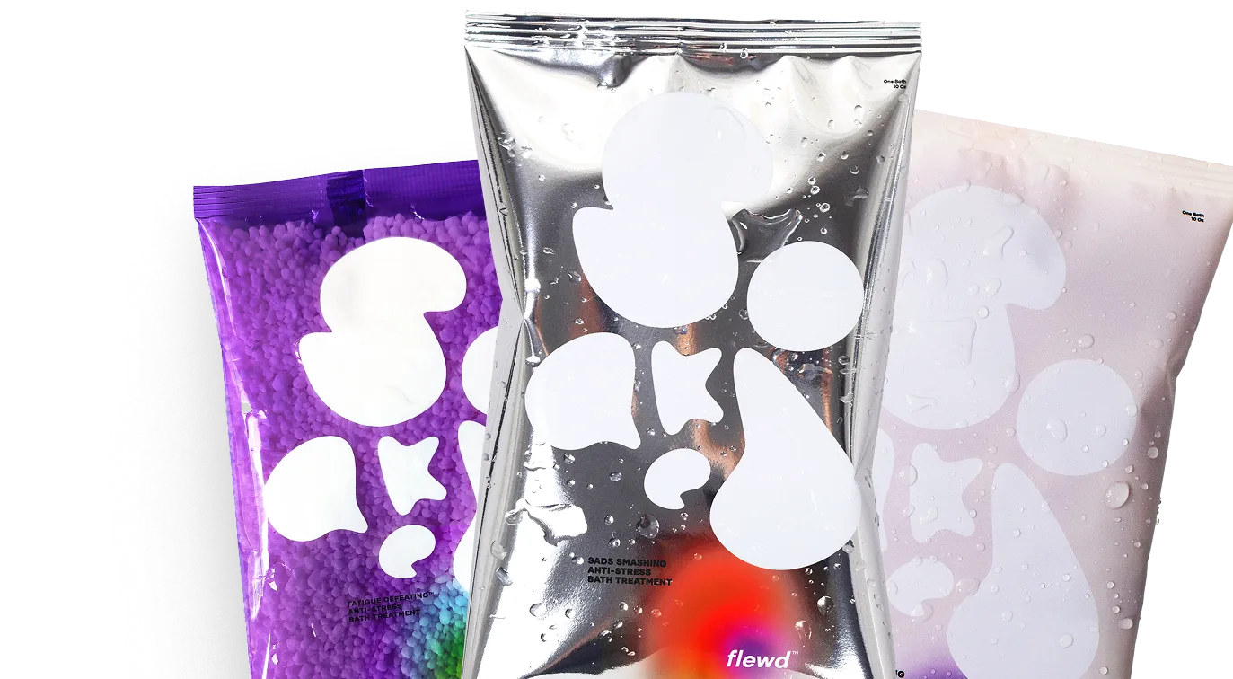 Three pouches of bath treatment products in purple, silver, and white packaging with abstract shapes and water droplets.