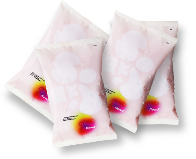 Four packets of flewd anti-stress bath treatment fanned out on a white surface with water droplets on them.