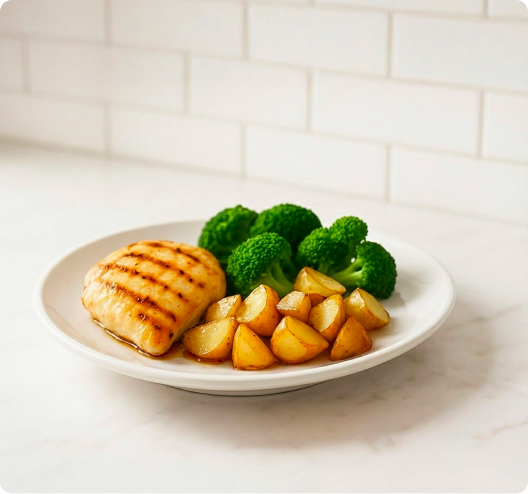A plate of grilled chicken breast, roasted potatoes, and steamed broccoli on a white countertop.