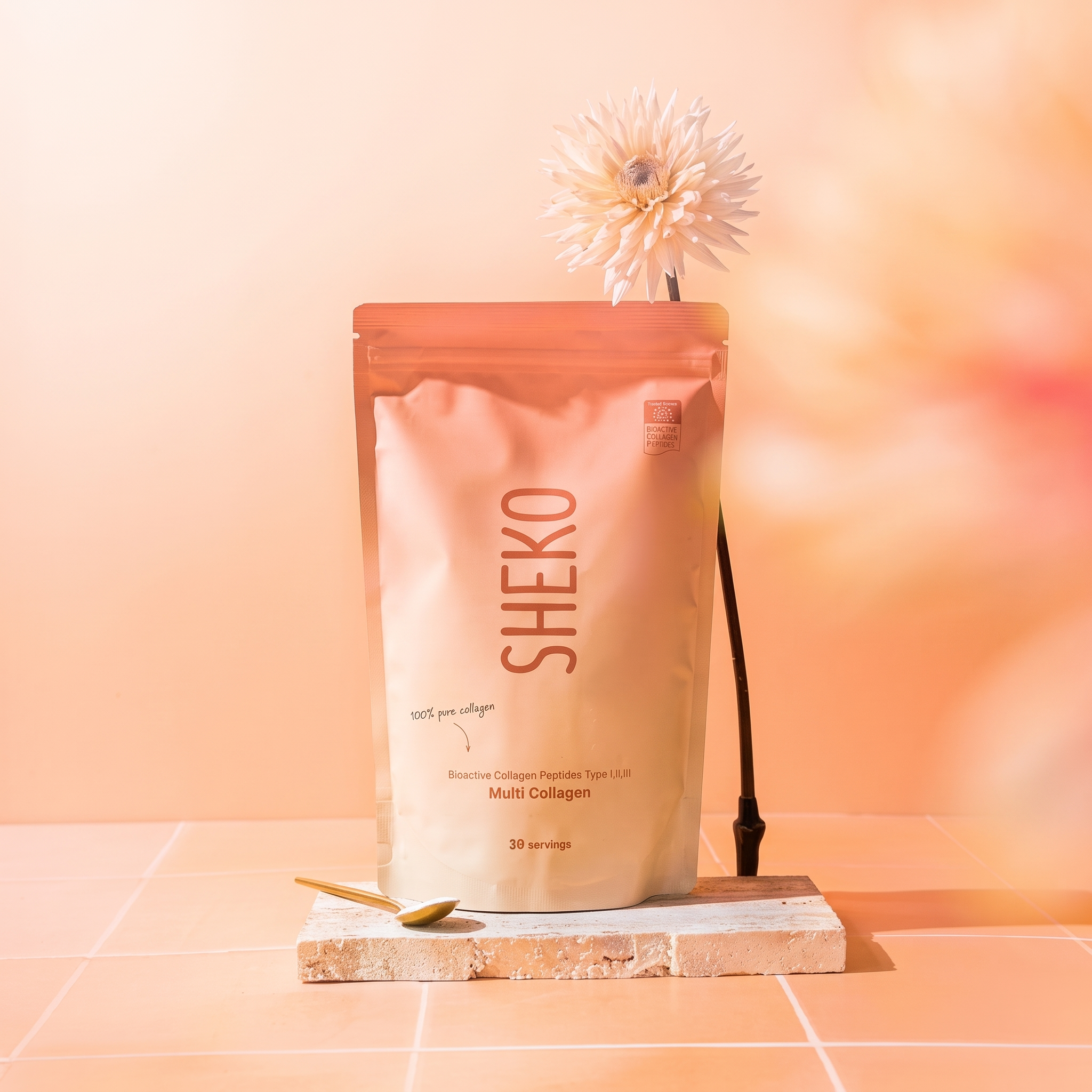 A pouch of SHEKO Multi Collagen powder sits on a stone block with a flower and a spoon.