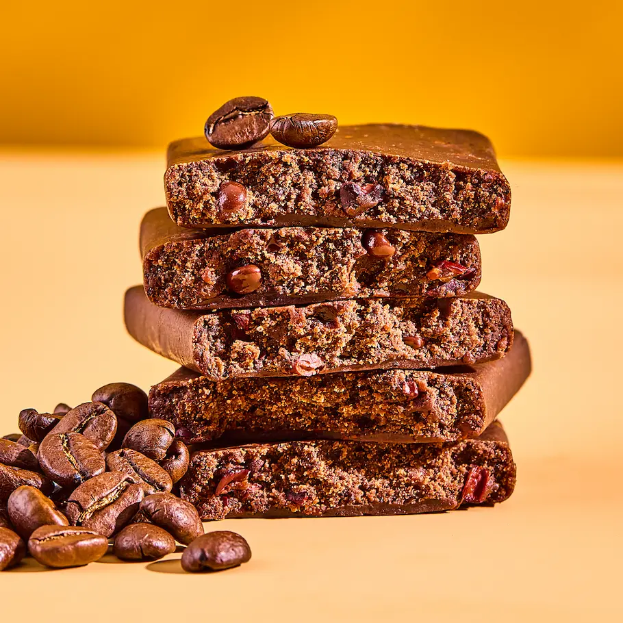 A stack of five cut coffee-flavored bars with whole coffee beans on a yellow background.