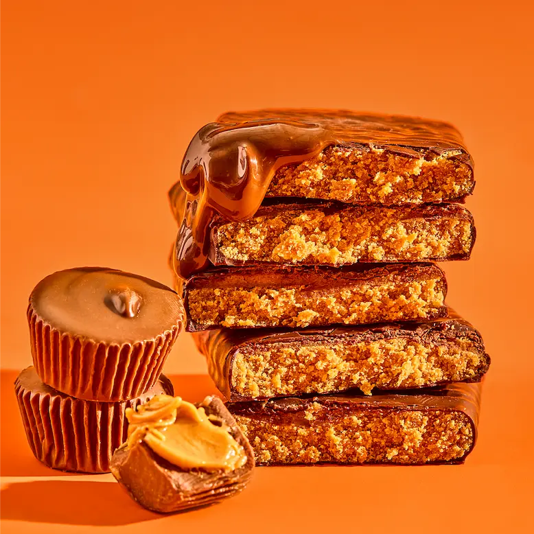 A stack of chocolate peanut butter bars with dripping caramel, next to chocolate peanut butter cups.