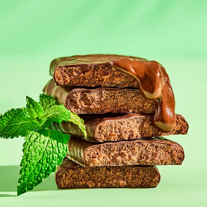A stack of chocolate-coated bars with melted chocolate dripping down, garnished with a sprig of fresh mint.