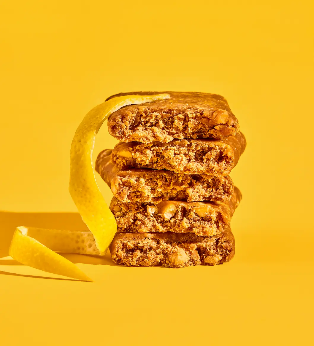 Stack of granola bars with lemon peel on yellow background.