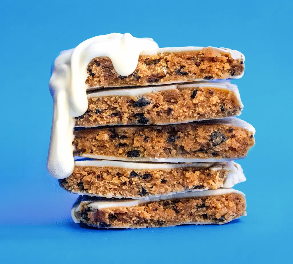A stack of five iced cookie bars with white frosting dripping down the side against a blue background.