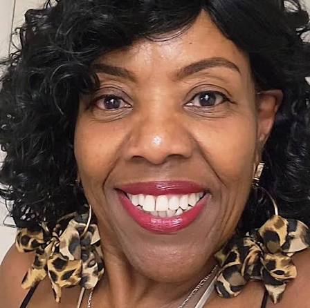 A close-up photo of a smiling Black woman with curly hair and large leopard-print earrings.