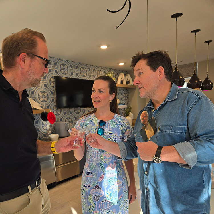 Three people standing and clinking small glasses together.