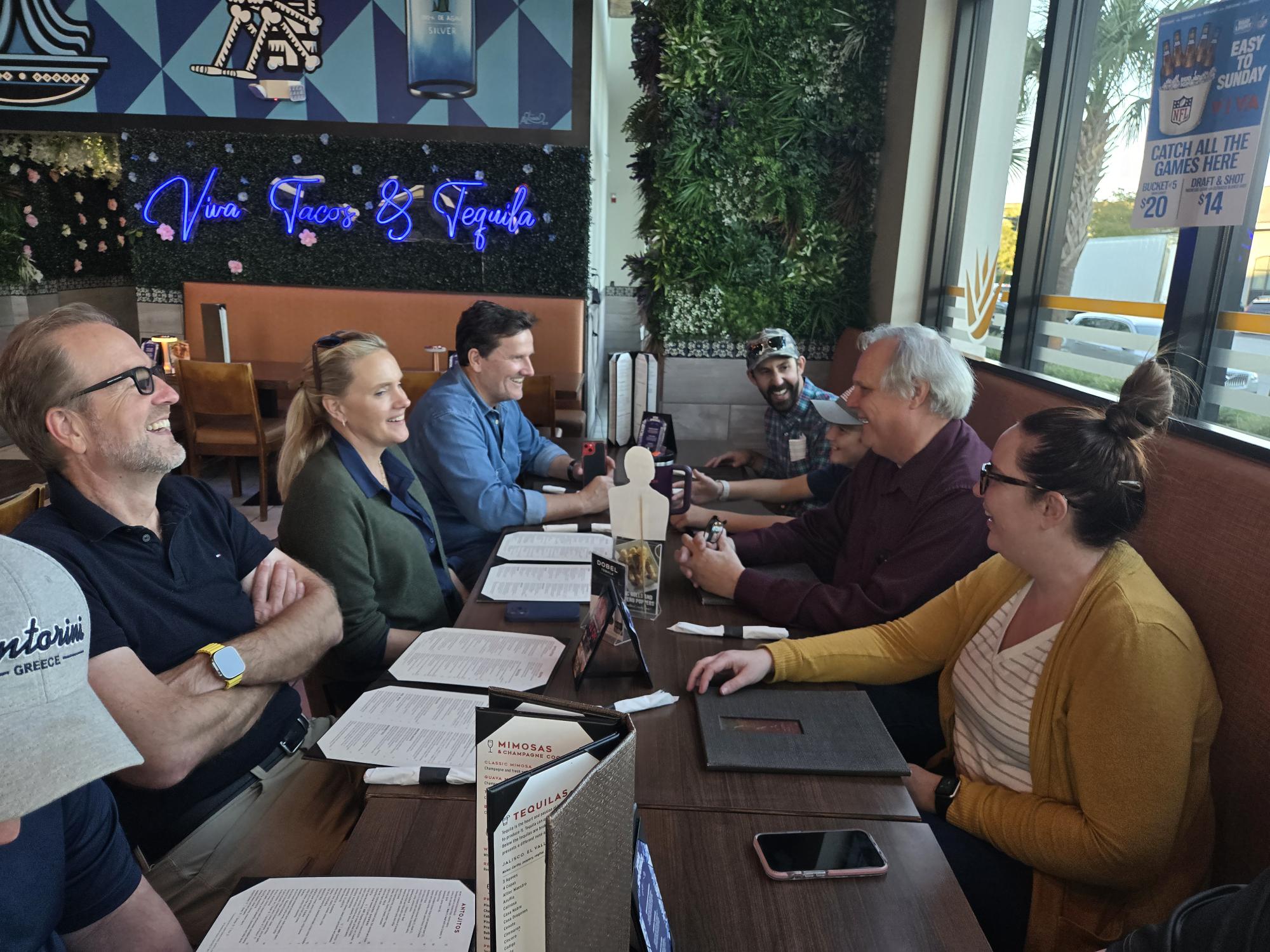 A group of people sitting around a dining table with dining menus smiling and laughing.