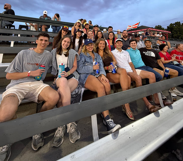  A group of people sitting on bleachers holding drinks.