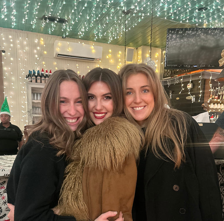 A group of women posing for the camera in a room filled with string lights and holiday decor.