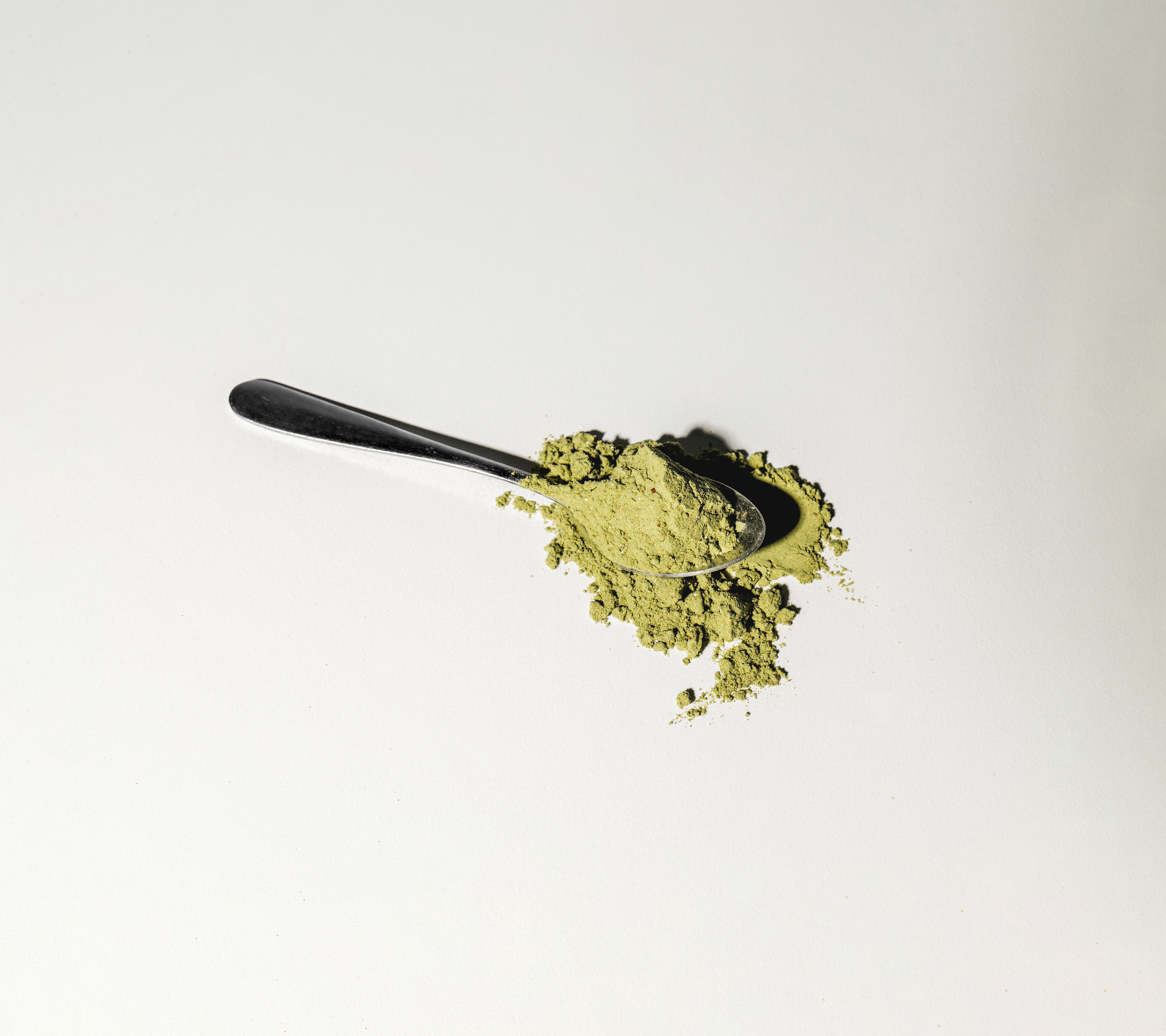 A silver spoon holding a scoop of green powder against a white background.