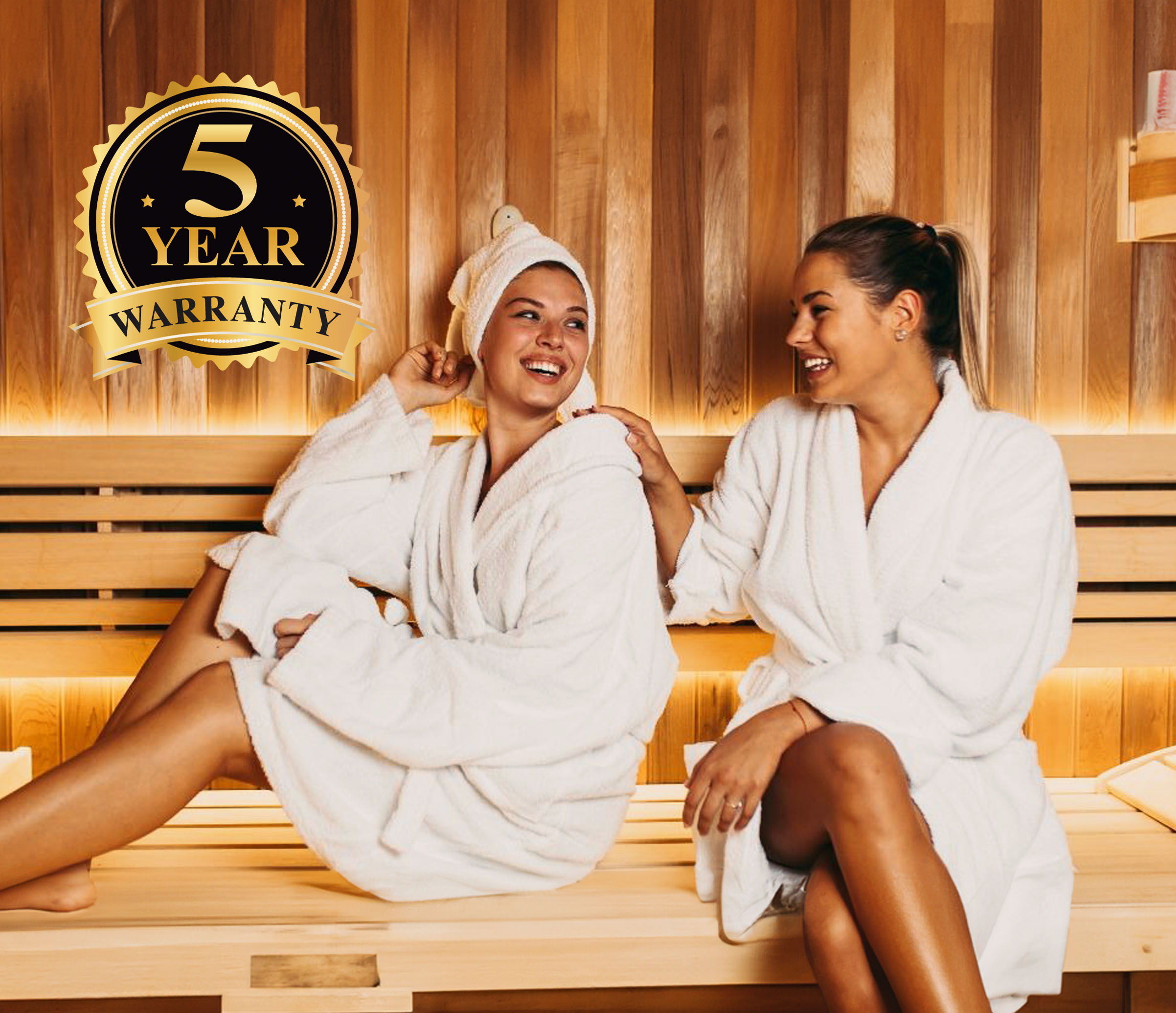 Two women in white robes sitting in a sauna, smiling.