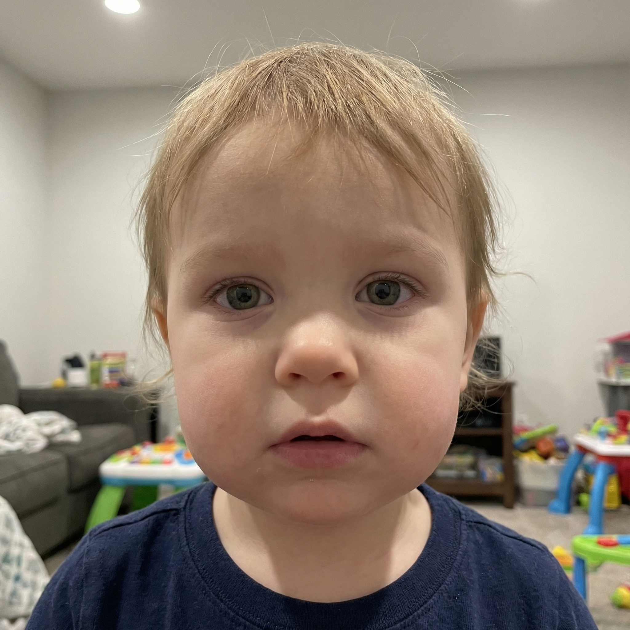 Close-up of a toddler in a room with toys and a couch.