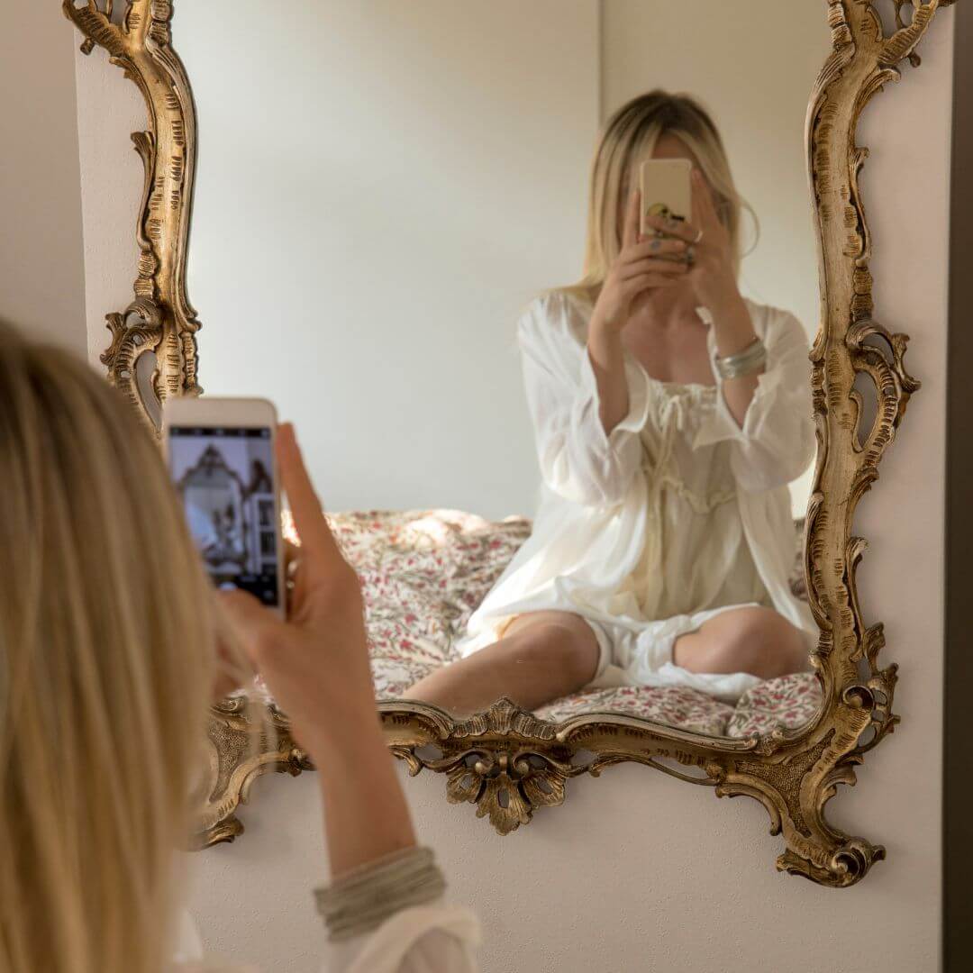 Person taking a mirror selfie with a smartphone in a decorative frame.