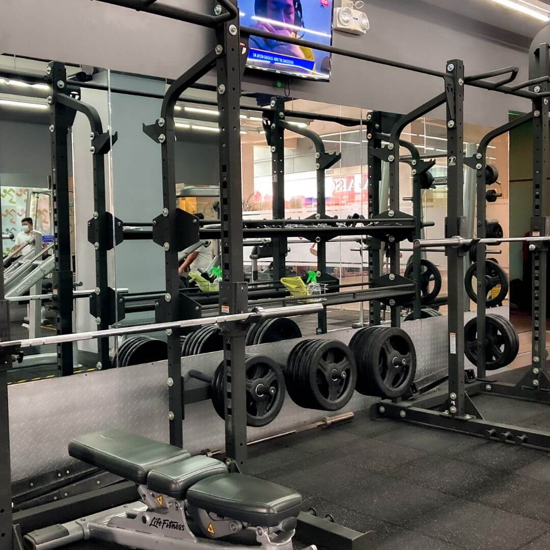 Gym with weightlifting equipment and a bench, mirrored walls, and a TV screen.