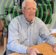 Elderly man sitting at a table, holding a remote, with concentric circles around him.