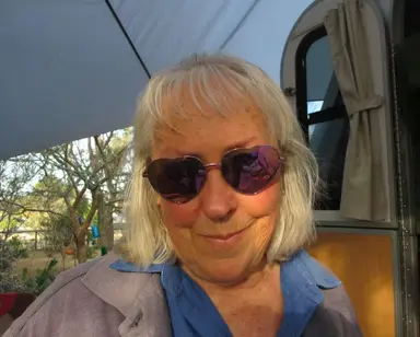 A woman with short, blonde hair and heart-shaped sunglasses smiling slightly at the camera.