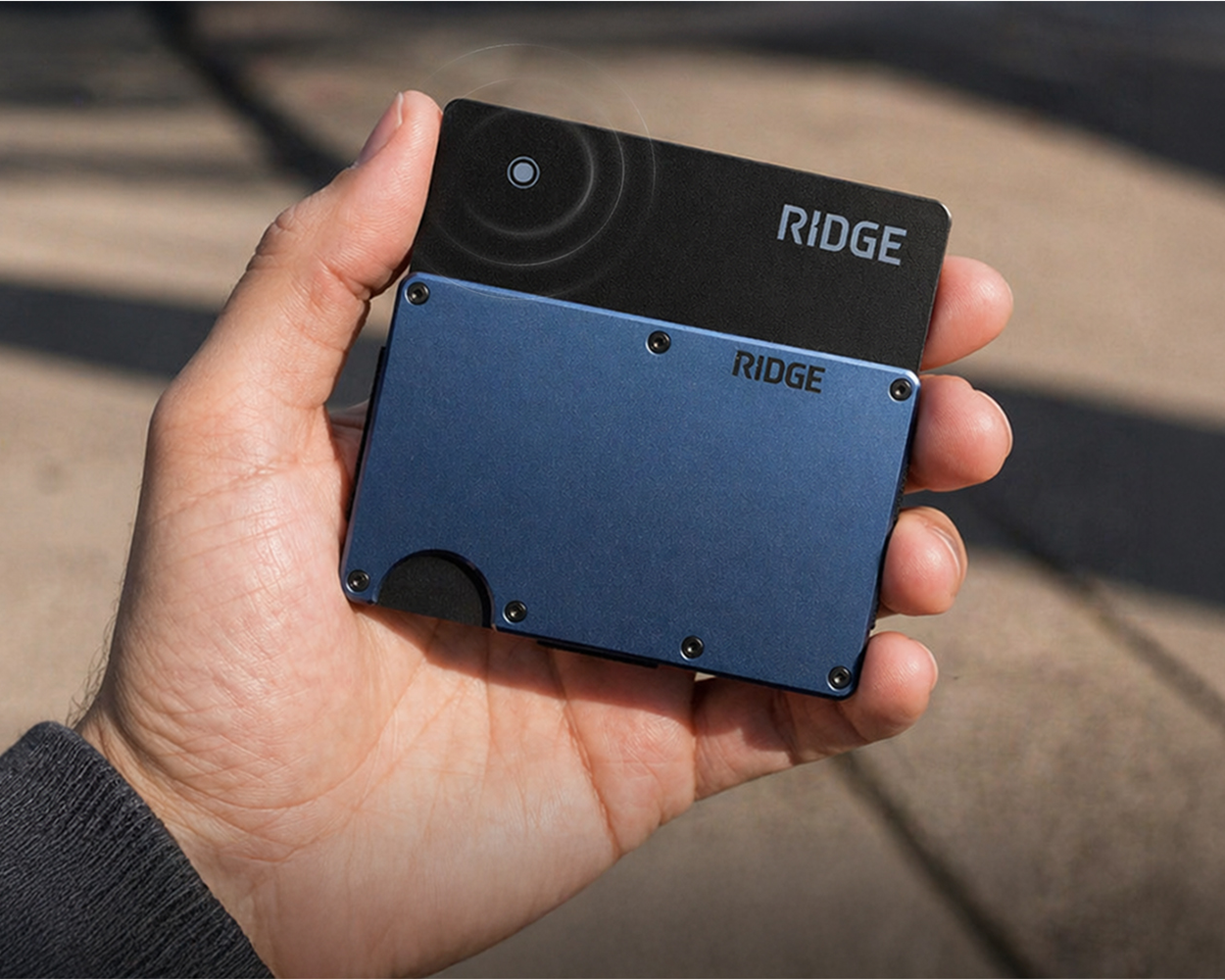 A person's hand holding a blue and black Ridge wallet with a card sticking out.