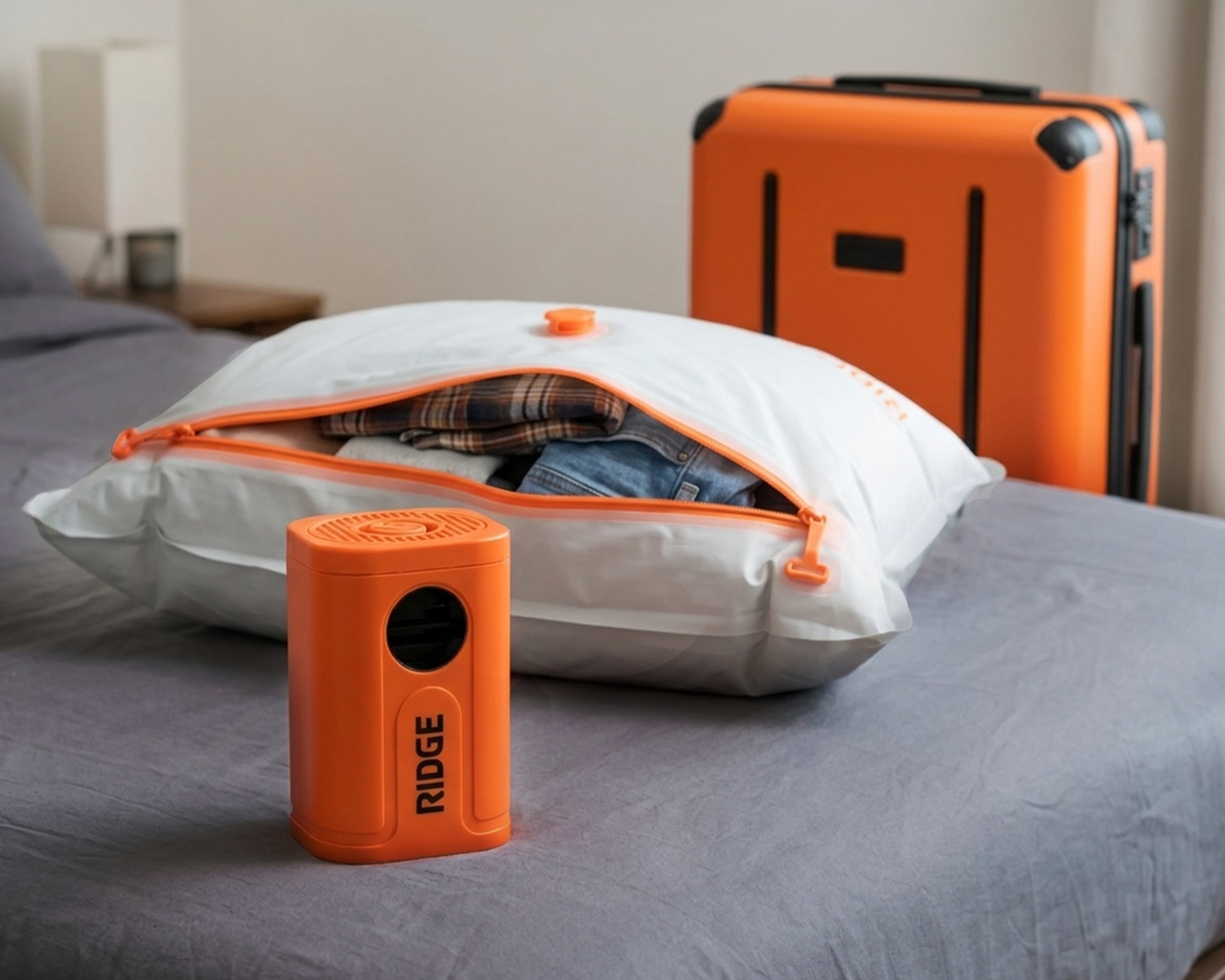 An orange portable vacuum pump and a vacuum-seal bag with clothes on a bed by a suitcase.