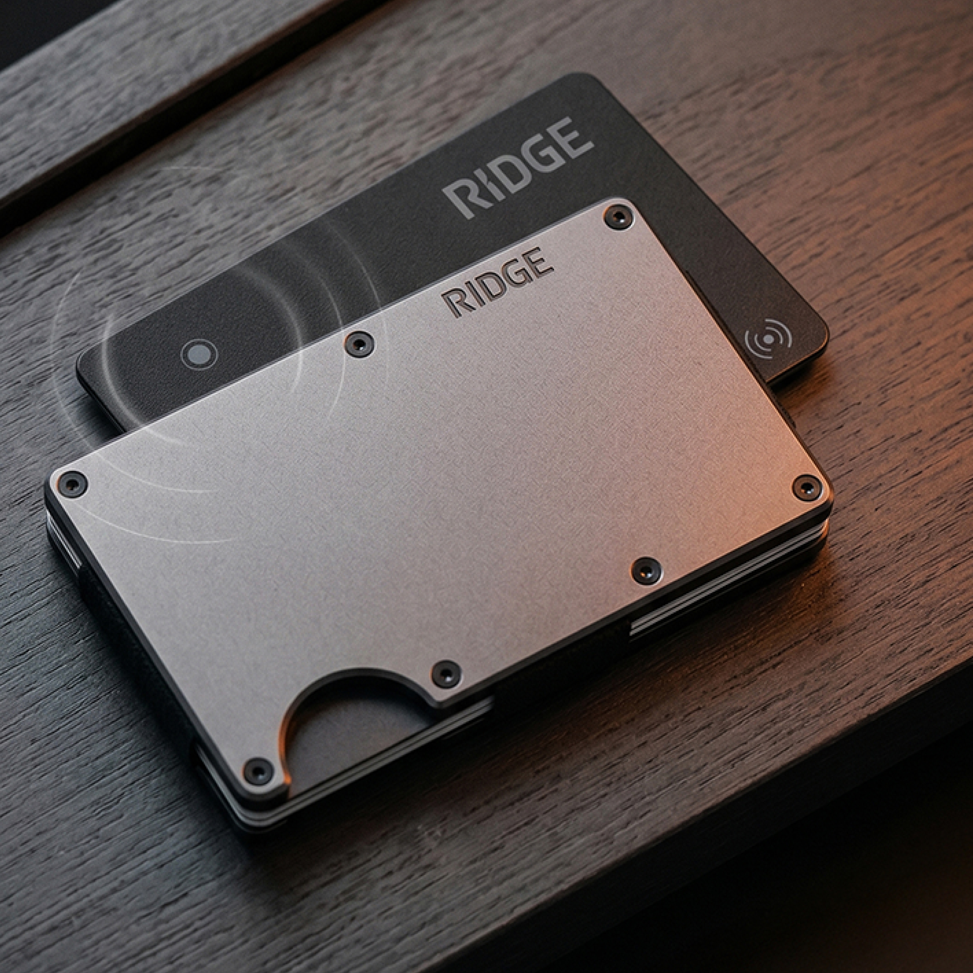 A silver Ridge wallet and a black Ridge card resting on a dark wood surface.