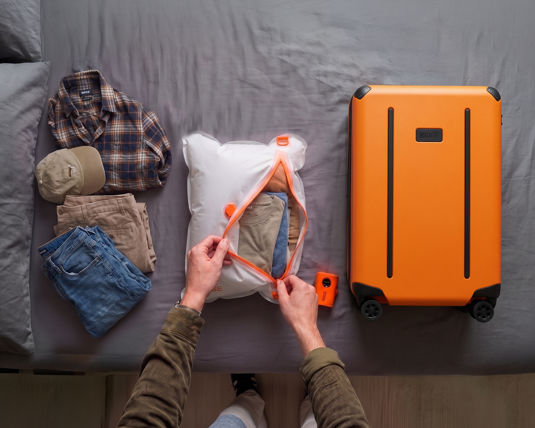 An overhead view of a person packing clothes into a cube next to an orange suitcase on a bed.