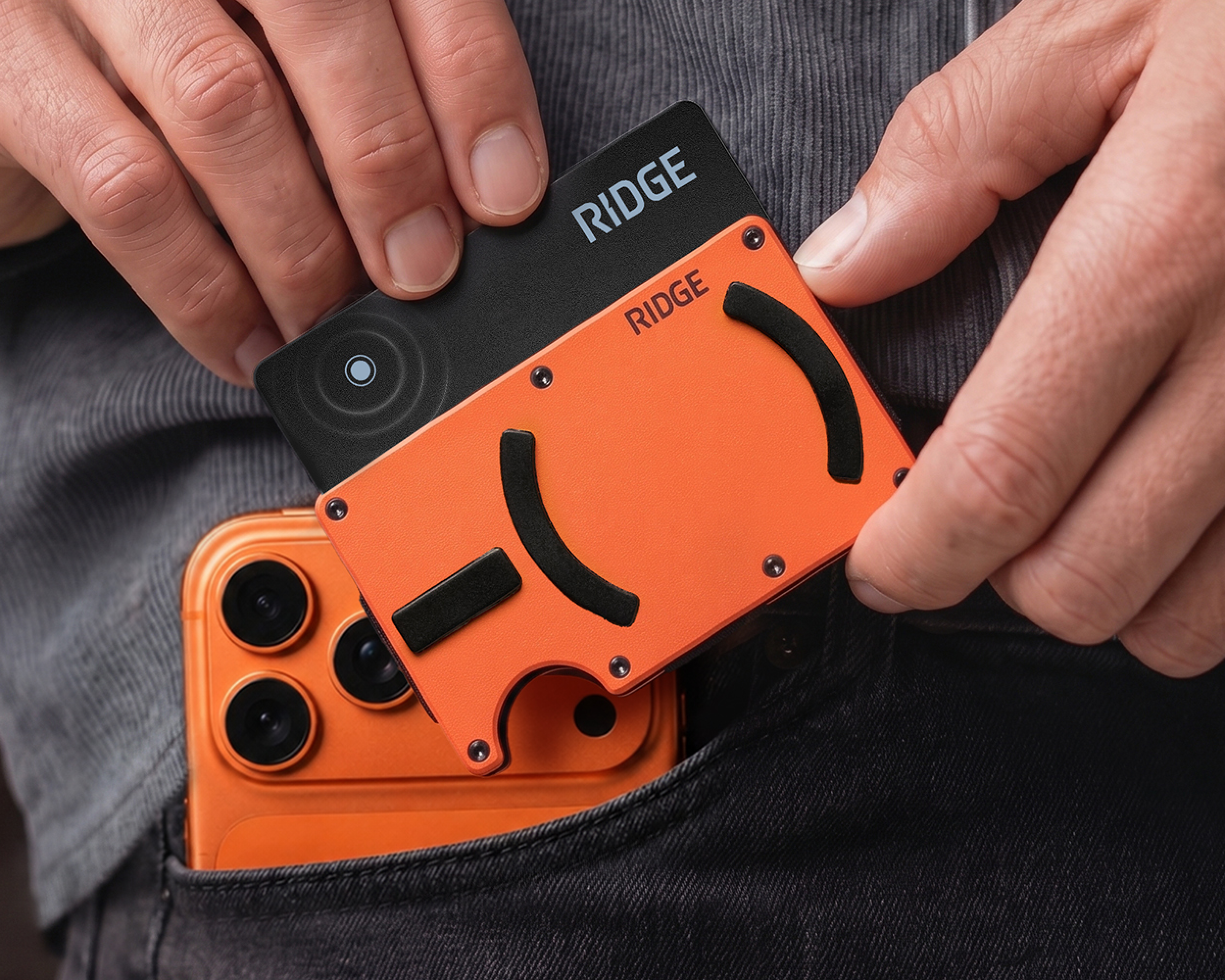 A person puts an orange wallet and a black card into a pocket with an orange phone.
