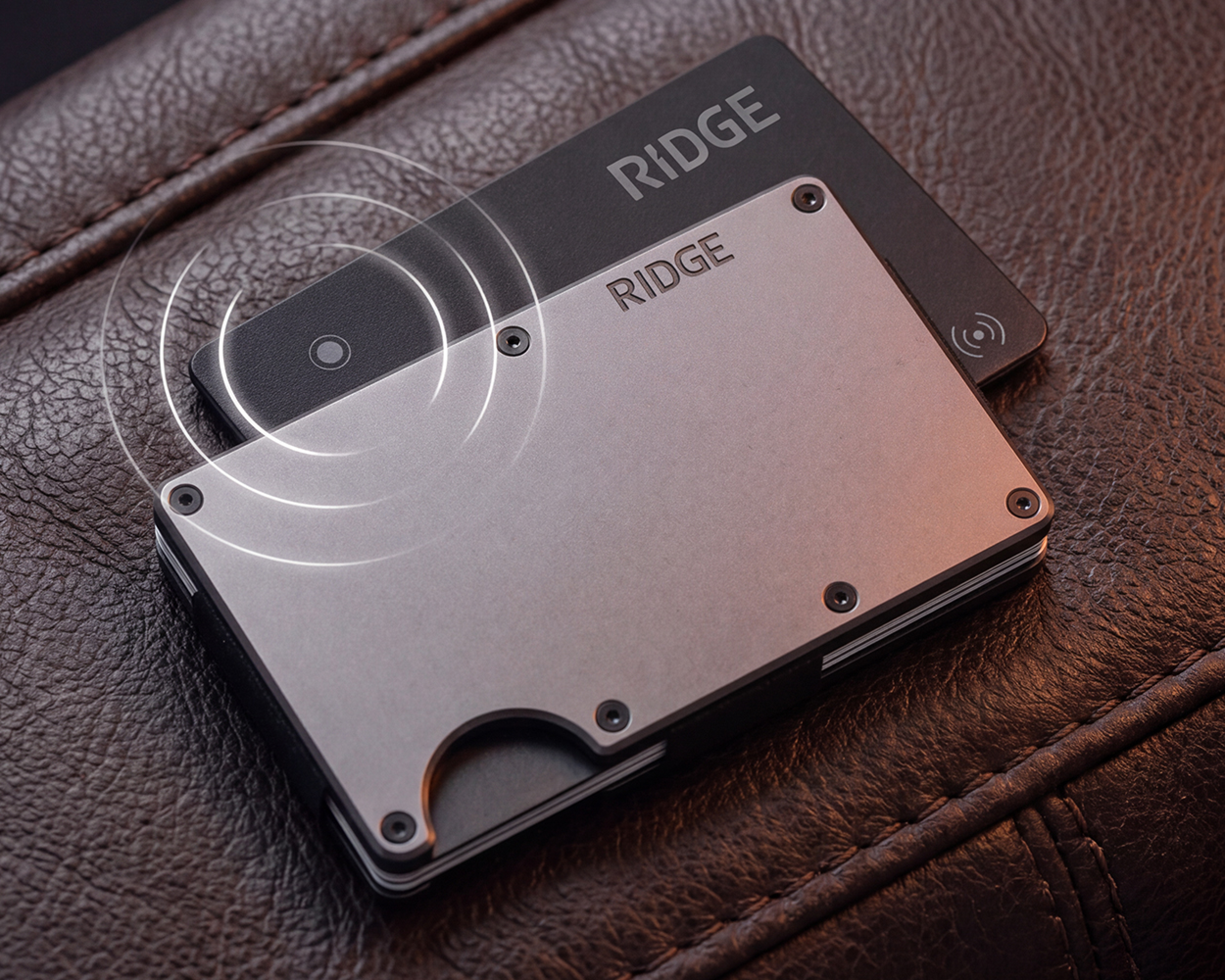 A silver Ridge wallet and a black smart card resting on a textured, brown leather surface.