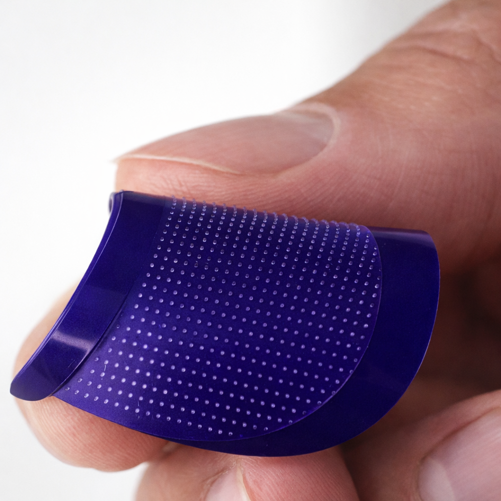 A person's fingers holding a small, flexible purple finger grip with a textured, dotted surface.
