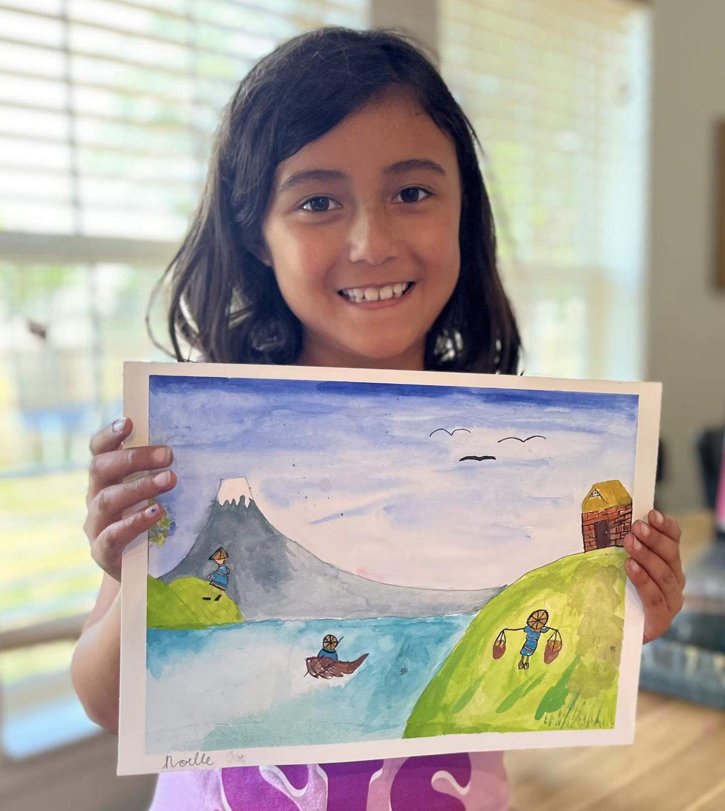 Child holding a colorful drawing of a landscape with mountains and water.