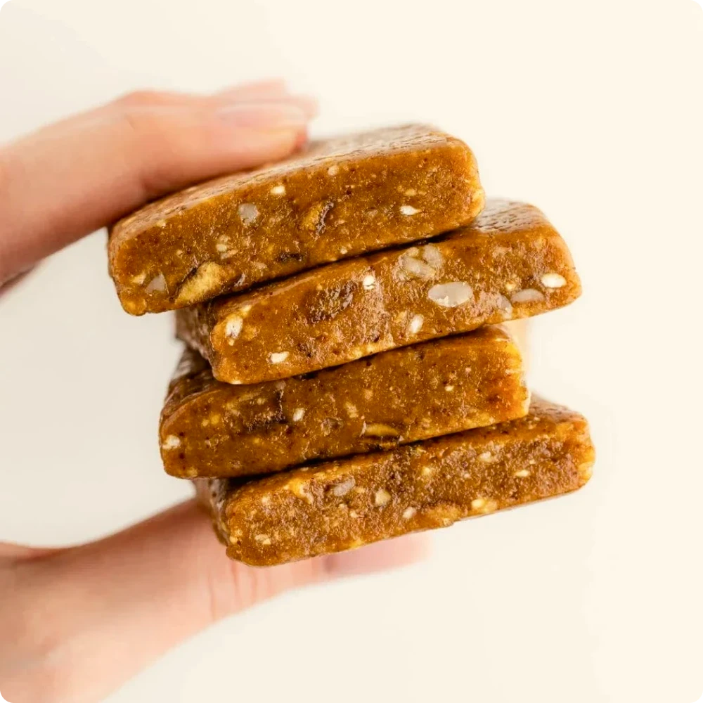 Hand holding a stack of chewy oat-based protein bars showing their soft texture and nut pieces