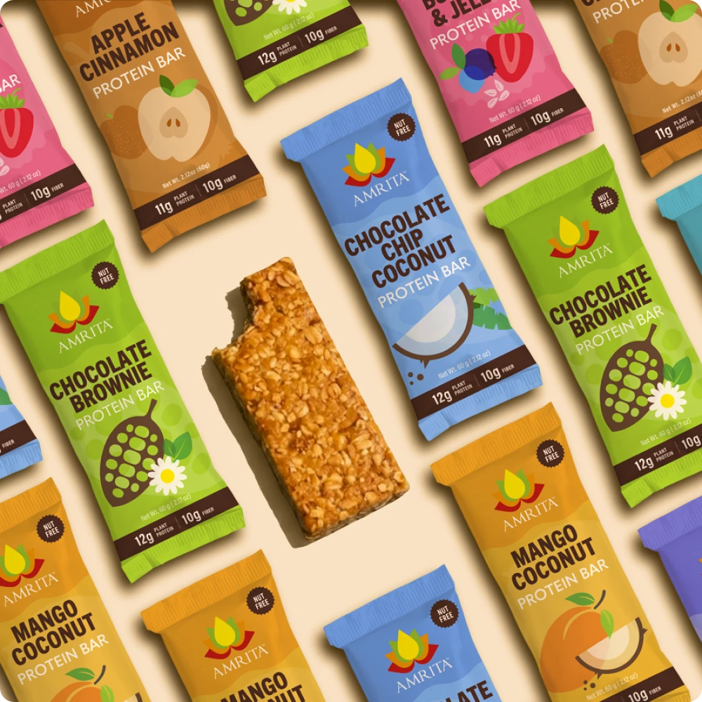Assorted Amrita protein bar packages arranged on a beige background with one unwrapped bar in the center