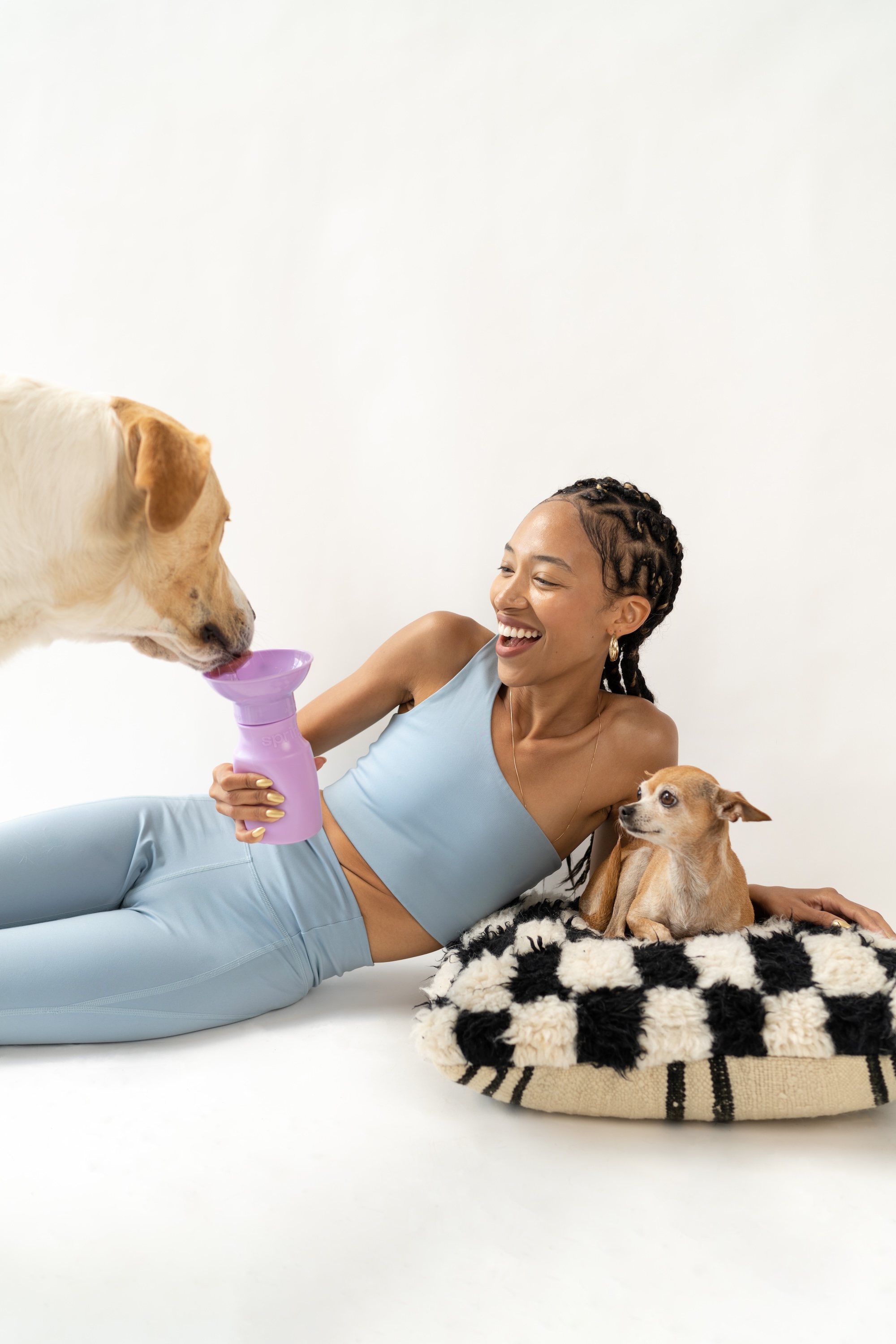 Woman in blue outfit with two dogs, one drinking from a purple container.