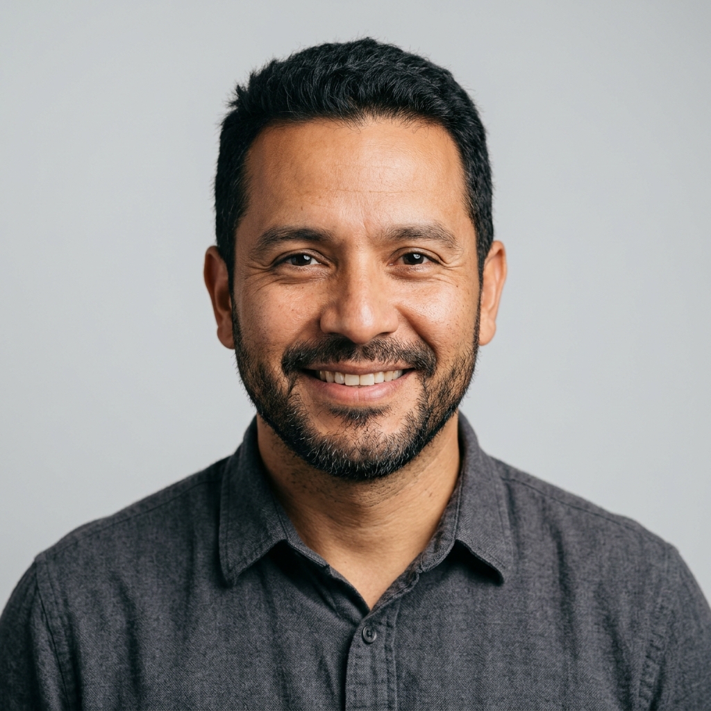 A headshot of a smiling man with a beard, wearing a gray collared shirt.