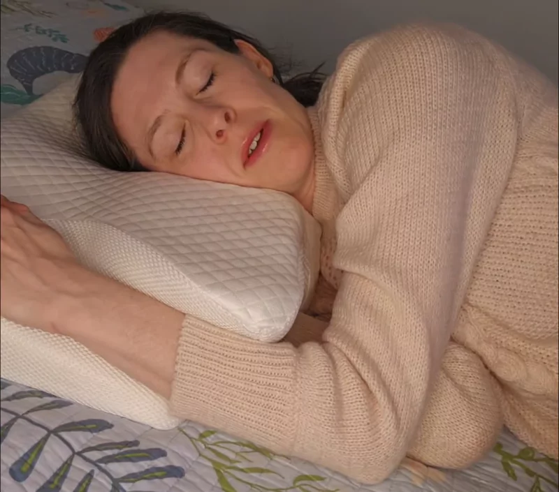 Man lying on a bed with a hand on his head, using a contoured pillow.