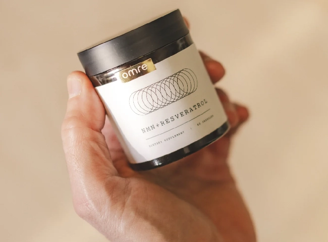 Hand holding a jar labeled 'NMN + Resveratrol' with a black lid.