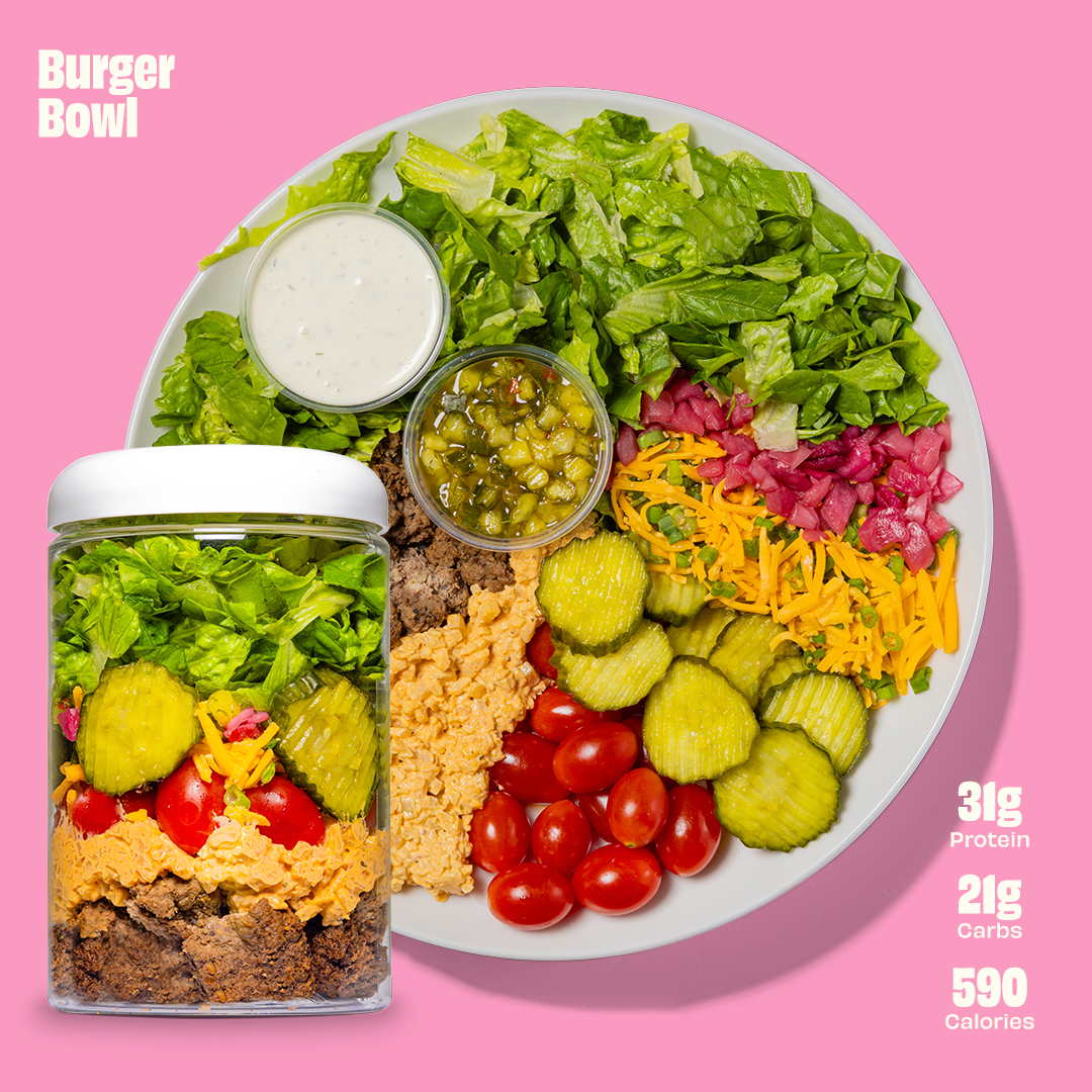A bowl with lettuce, cheese, pickles, tomatoes, ground beef, and two small containers of dressing.