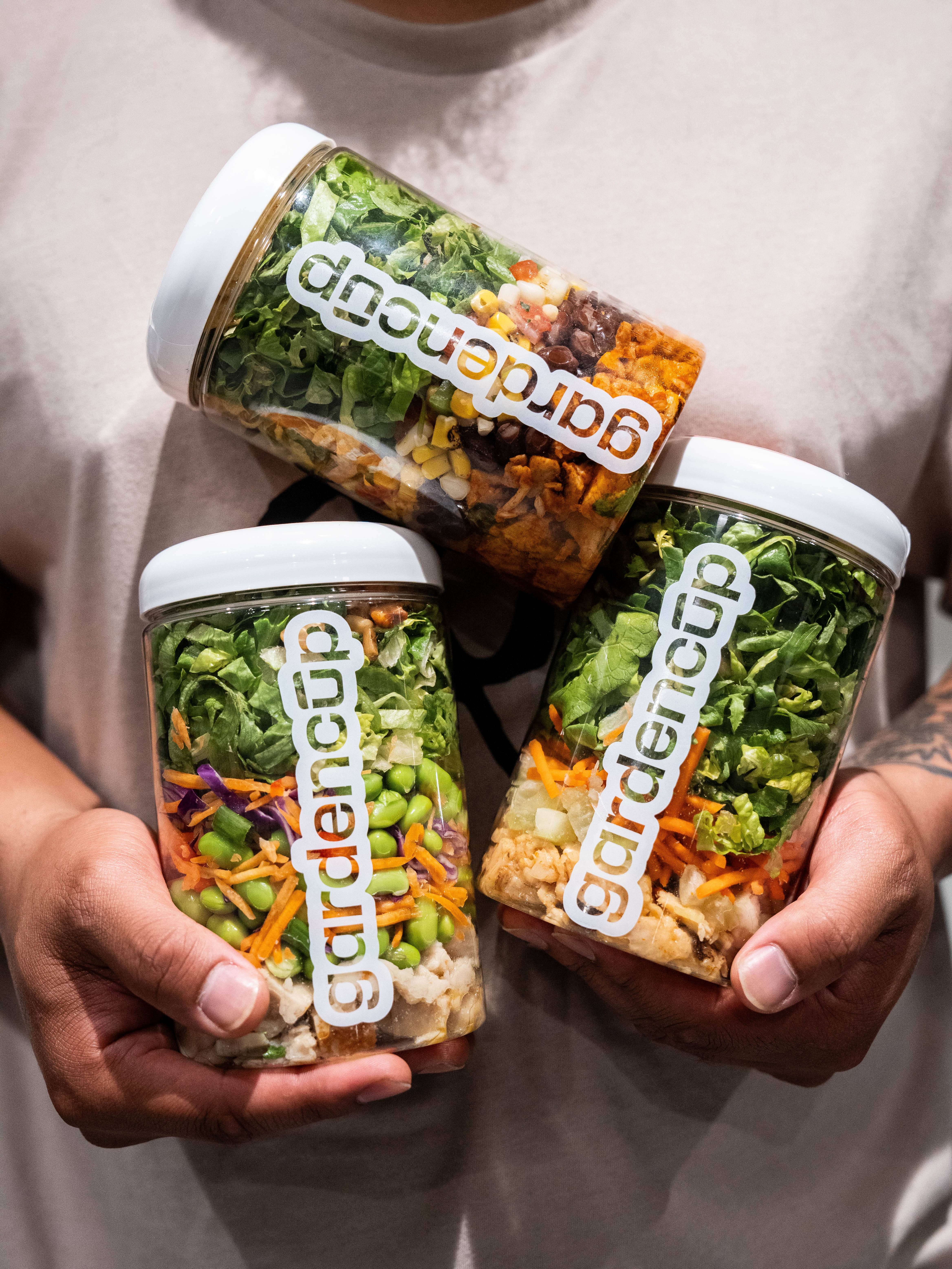 Person holding three jars of layered salads labeled 'gardencup.'